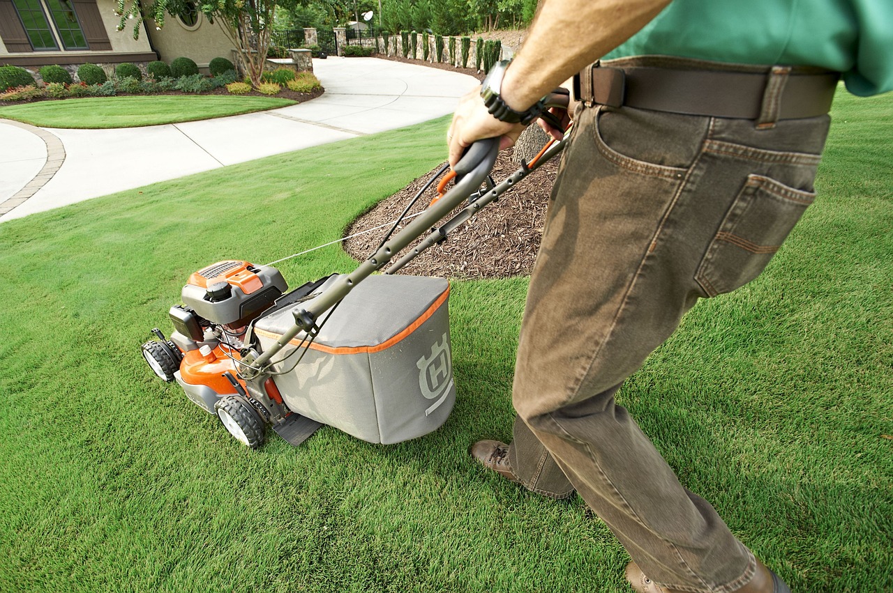Lawn mowing services Wellington: Man mowing a green lawn with a Husqvarna mower.